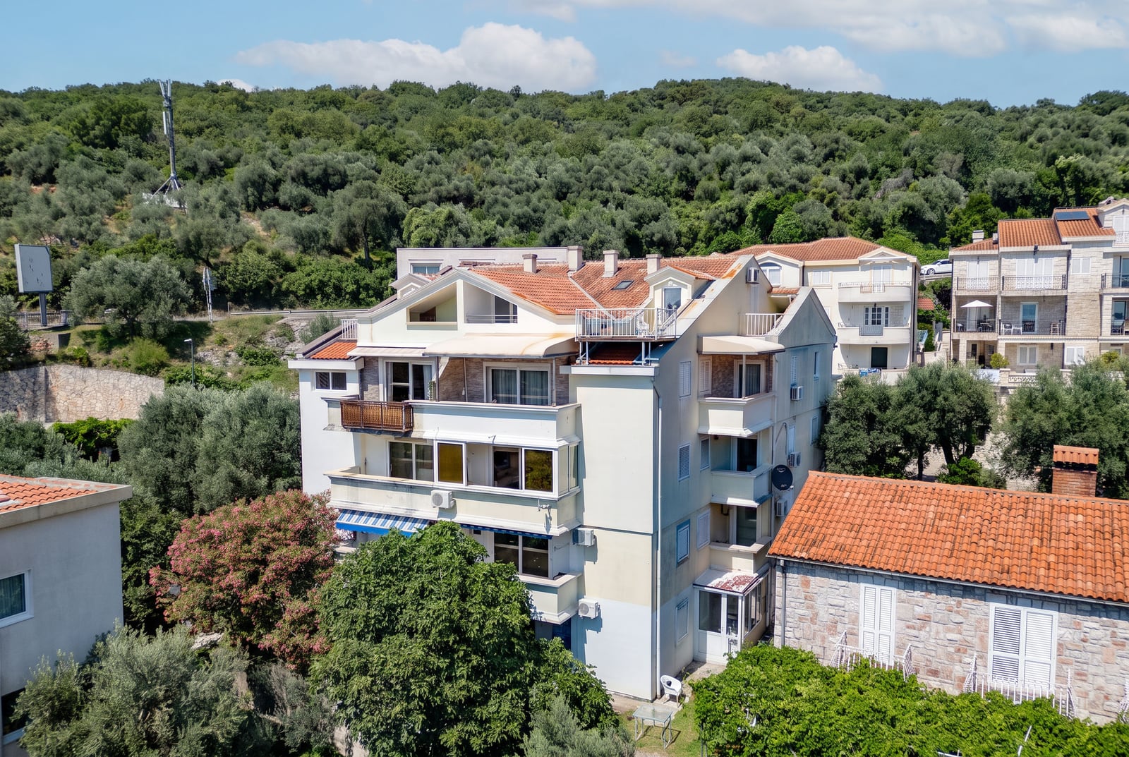 Three-story residential building with terraces surrounded by greenery, Sveti Stefan, Montenegro: view of the building facade with a tiled roof.