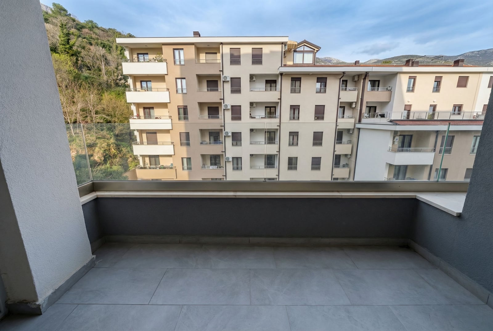 Pogled sa balkona modernog stana u Bečićima, Crna Gora: panoramsko zastakljenje, pločice na podu i pogled na stambeni kompleks.