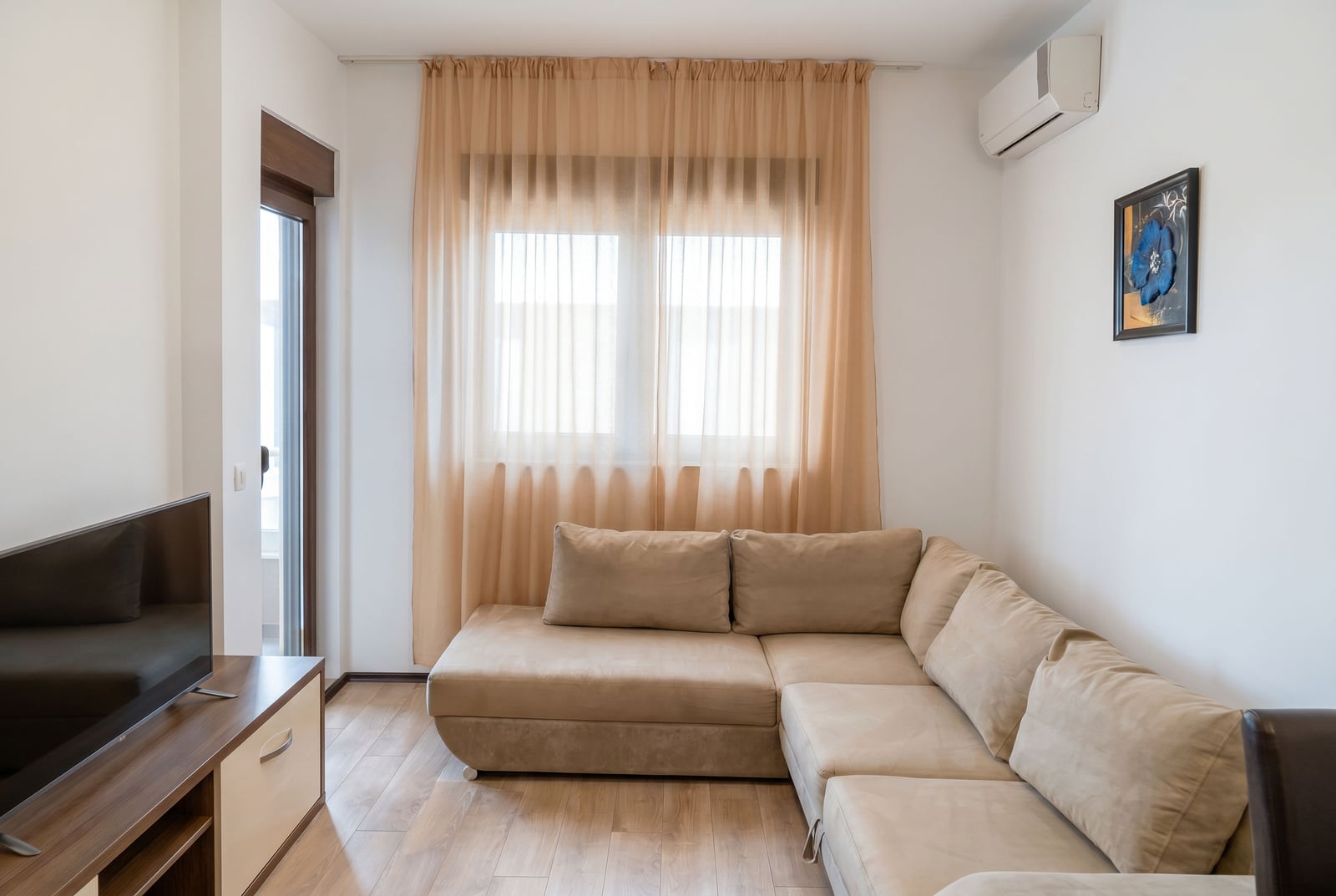 Cozy living room with a beige sectional sofa and TV area in a Budva apartment, Montenegro. Bright interior with air conditioning.