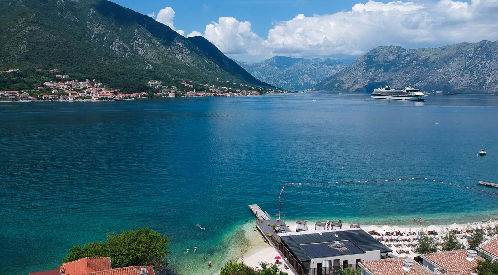 Panoramablick auf die Bucht von Kotor und den Strand von der Terrasse der Villa in Dobrota, Montenegro: Meer, Berge und ein Kreuzfahrtschiff.