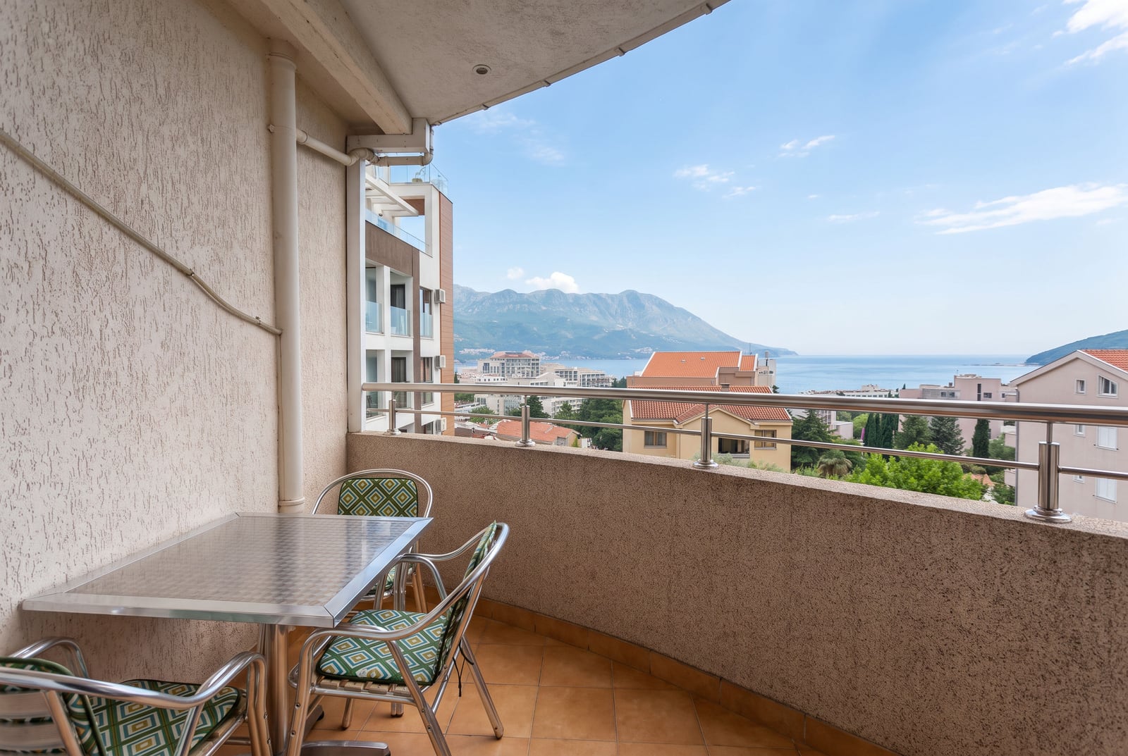 Apartment balcony in Becici, Montenegro, with a dining table, chairs, and a panoramic view of the sea and mountains