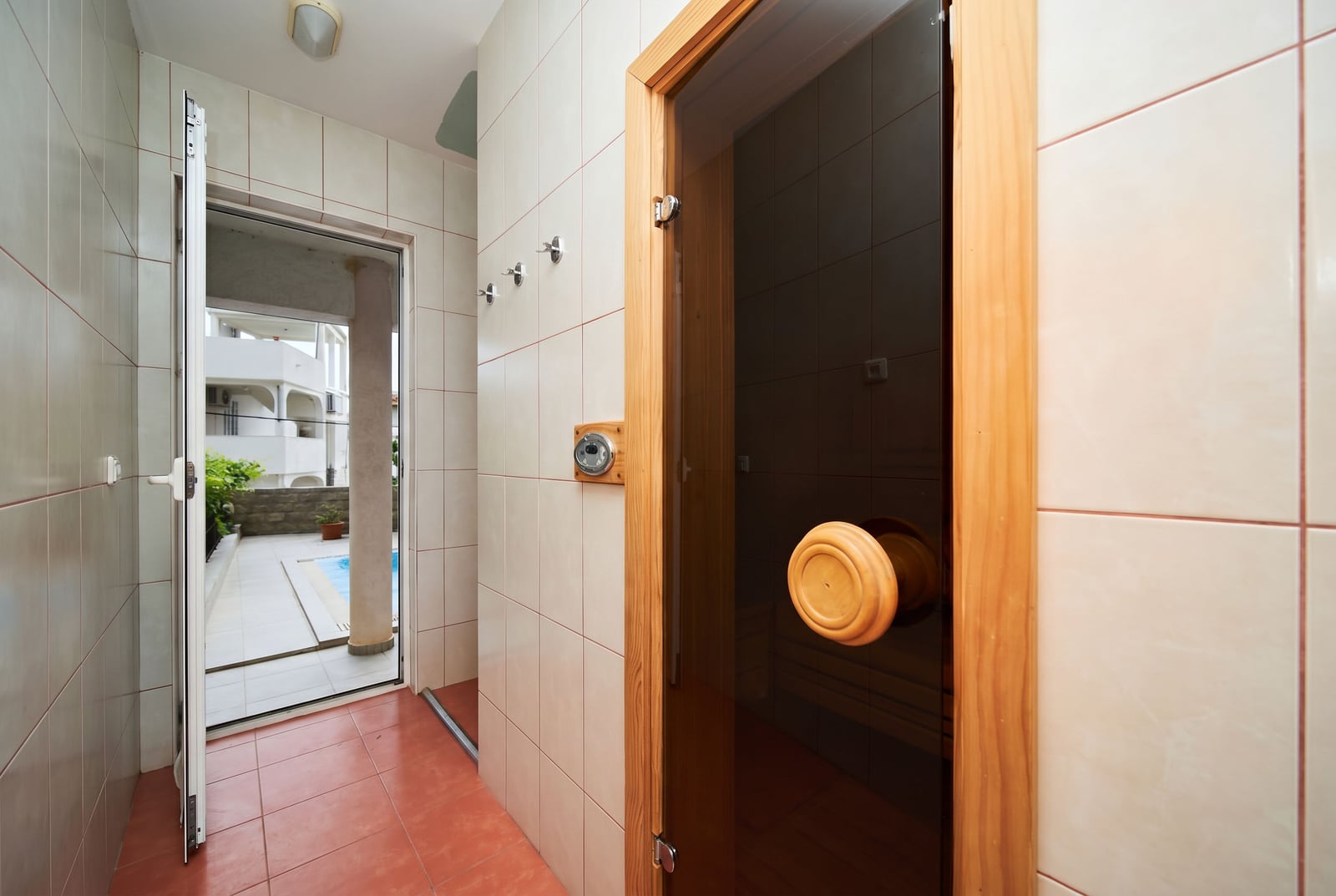 Salle de bain avec sauna et accès à la piscine dans une villa à Bečići, au Monténégro. Finitions en carrelage et porte en bois.