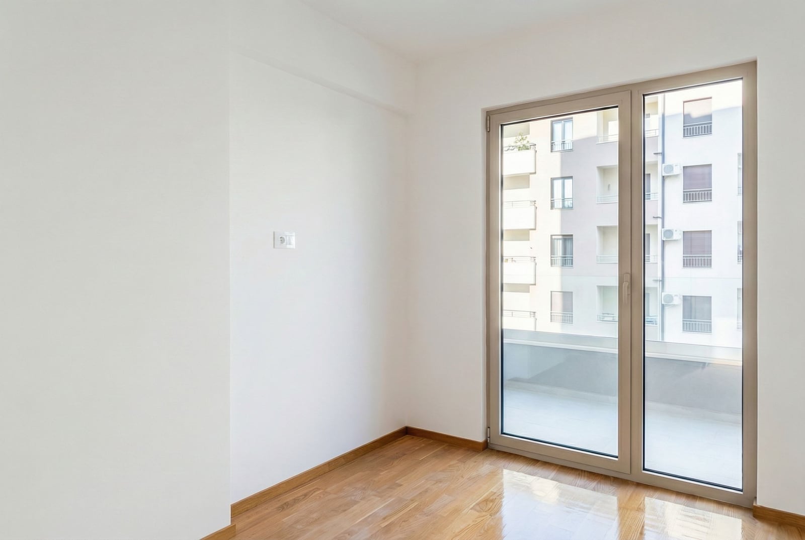 Svetla prazna dnevna soba sa parketom i izlazom na balkon u stanu u Bečićima, Crna Gora.