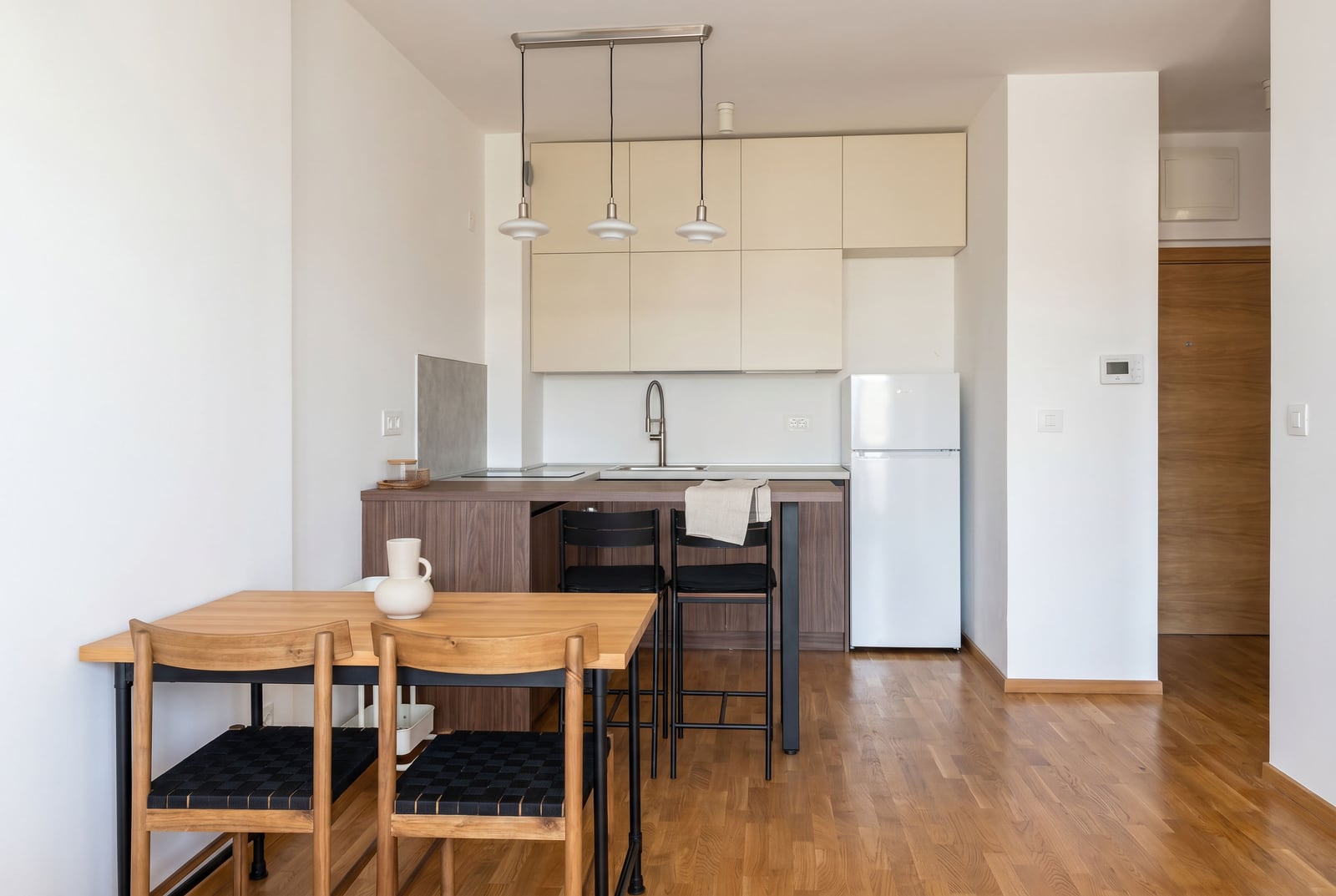 Modern open-plan kitchen with a dining area in a Becici apartment, Montenegro: light-colored cabinetry, wooden flooring, and furniture.