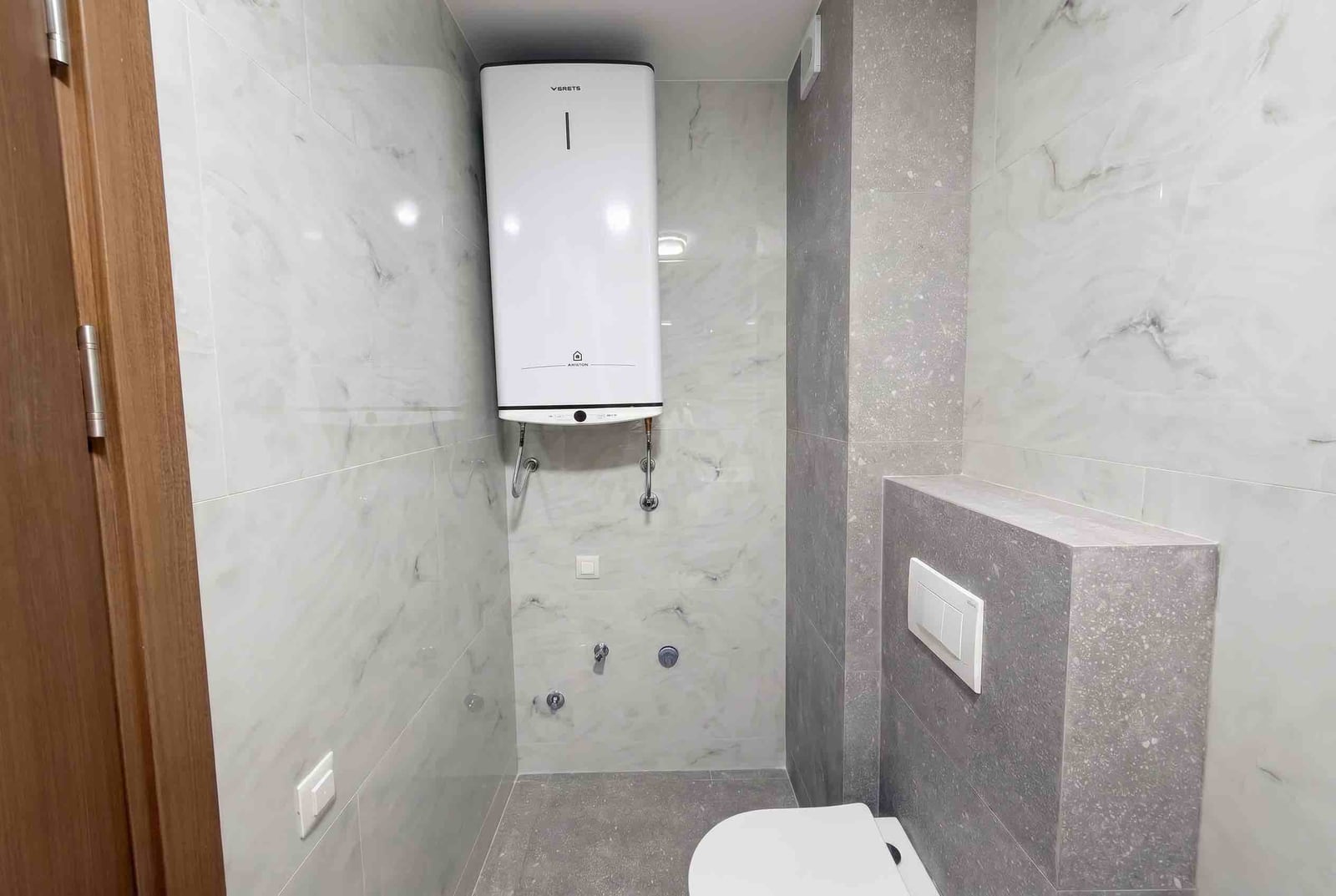 Modern bathroom in an apartment in Budva, Montenegro: light marble-look tiles and an electric water heater.