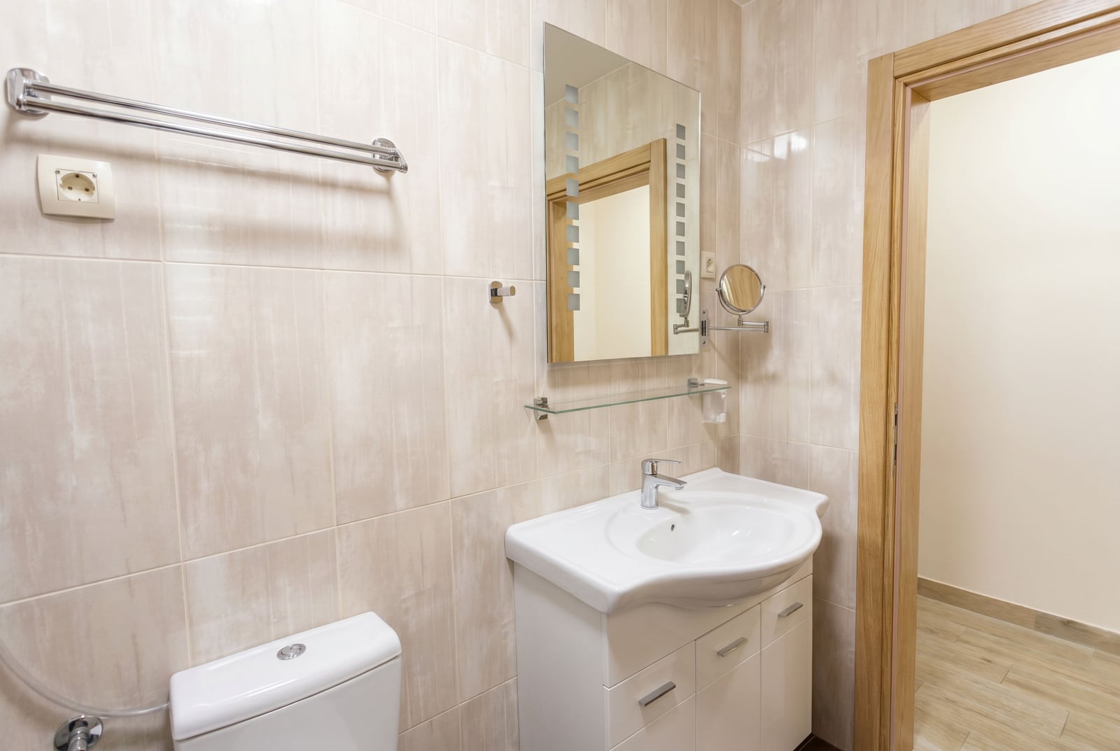 Bright bathroom in an apartment in Bečići, Montenegro: white vanity with a sink, mirror, and beige tiles.