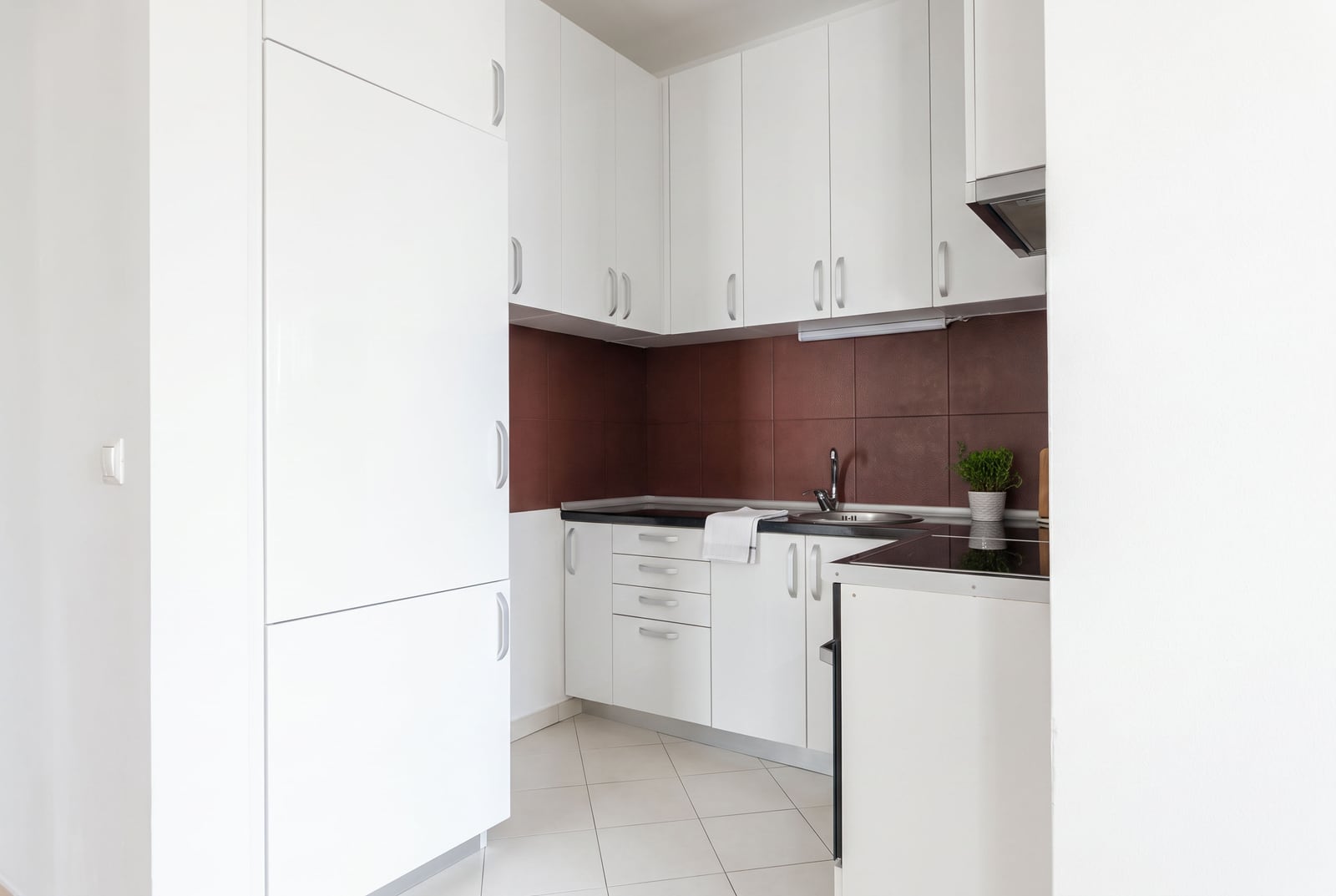 Moderne weiße Küche mit Möbeln, eingebauten Geräten und brauner Rückwand in einer Wohnung in Budva, Montenegro