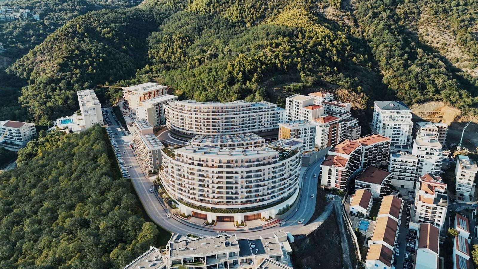 Karadağ, Bečići’deki konut kompleksinin havadan görünümü: yeşil dağlar ve ormanlar арасында modern çok katlı binalar.