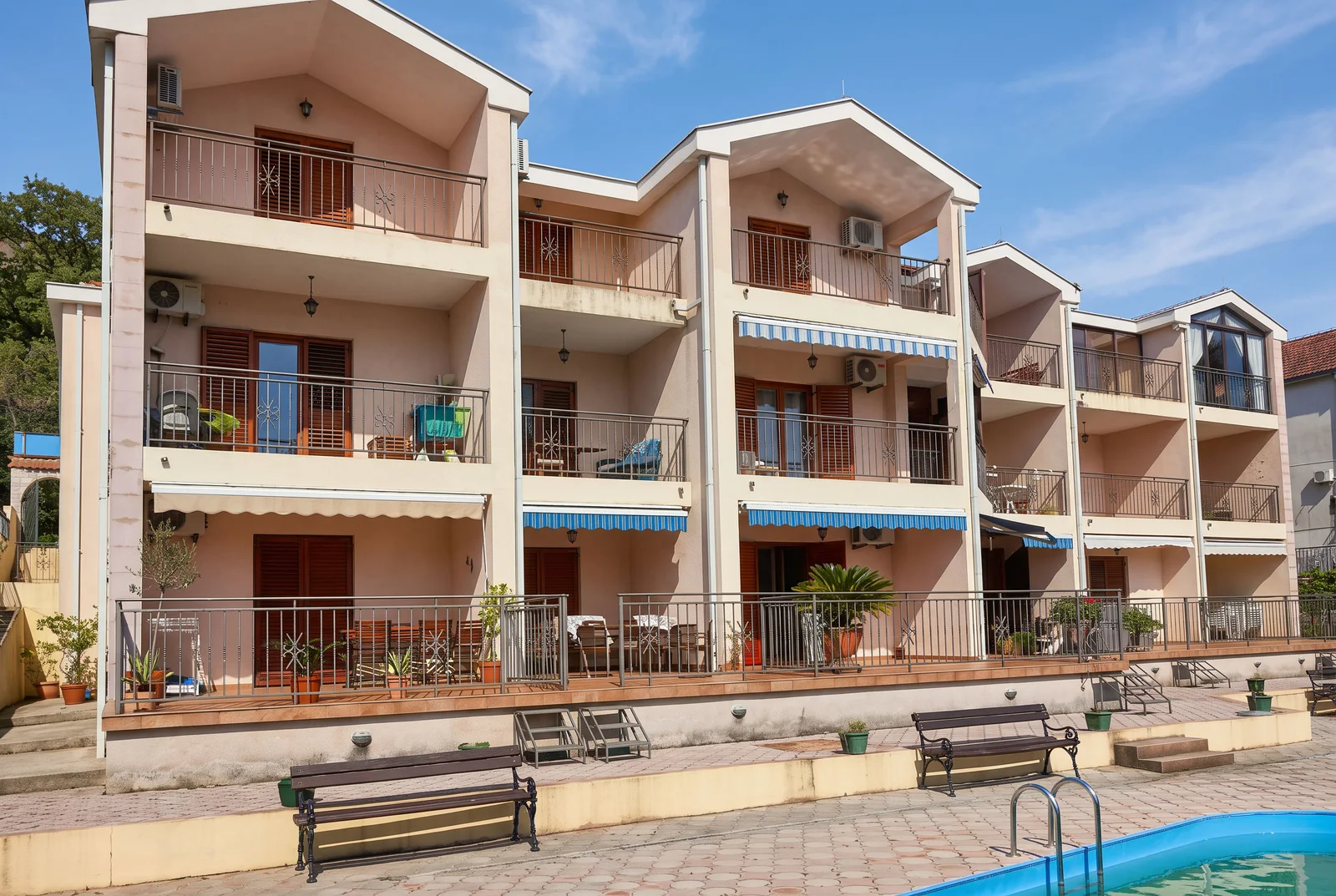 Vue extérieure d'un bâtiment à plusieurs étages avec balcons, terrasse et bord de piscine au premier plan.
