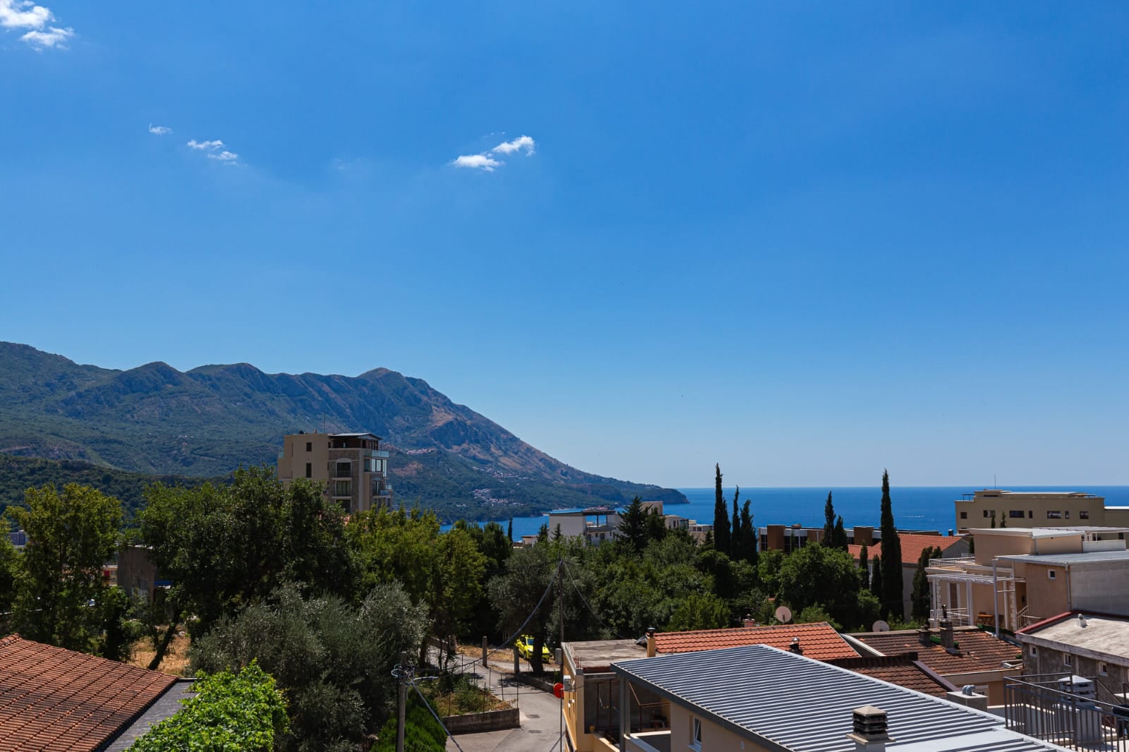Vue panoramique sur la mer et les montagnes depuis la terrasse d'une villa à Bečići, au Monténégro : paysage pittoresque avec toits de maisons et verdure.
